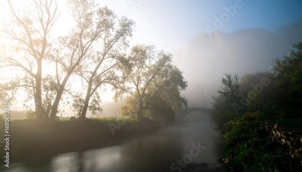 Fototapeta Misty dawn over a tranquil river, arched bridge, and silhouetted trees