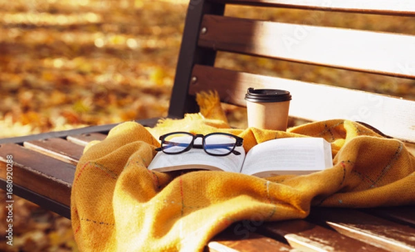 Fototapeta Open book with eyeglasses placed on a warm blanket outdoors on a bench in autumn park. Cozy fall atmosphere, reading, studying, and relaxation concept. Selective focus.