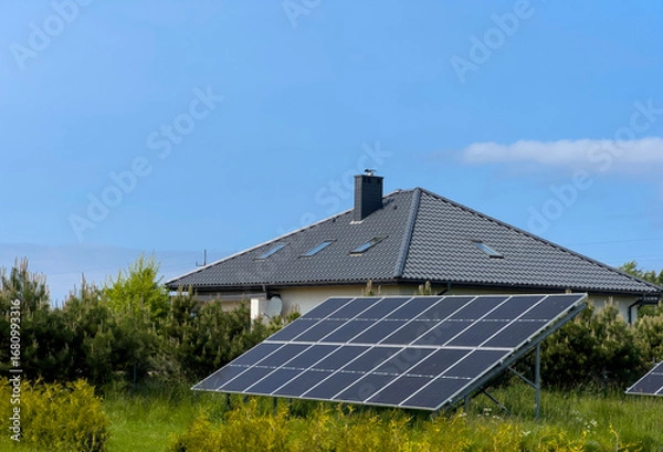 Obraz A modern country house with solar panels in the garden outside the fence in the green.