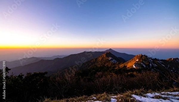 Fototapeta Panoramic sunset view of a mountain range, showing layers of peaks and valleys, with a hint of snow near the foreground
