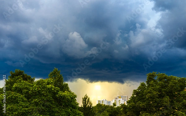 Fototapeta Ominous thunderclouds over landscape with trees and city buildings