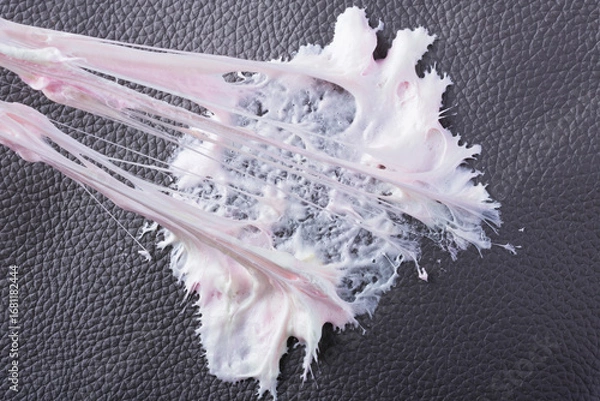 Fototapeta Chewing gum has become stuck to a dark textured surface, showing its stretching and gooey consistency. The leather surface shows intricate texture as the cleaning care. Daily stains concept