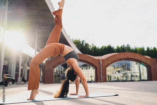Fototapeta Athletic woman practicing advanced yoga inversion outdoors with arched back. Conceptual fitness image representing empowerment, mindfulness, resilience, strength, flexibility, and balanced lifestyle.