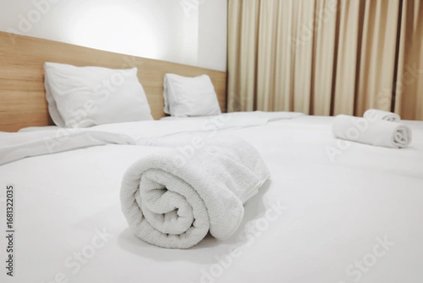 Fototapeta A neatly rolled white towel is placed on a fresh, clean bed with crisp white linens, symbolizing hospitality and comfort.