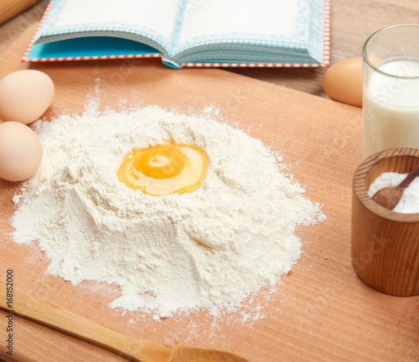 Fototapeta Flour heap and broken egg closeup for baking on a wooden background. Raw food and kitchen utensils.