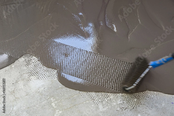 Fototapeta Spreading self leveling plaster with a special roller. Interior