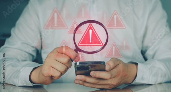 Fototapeta Man holding smartphone with red warning icons indicating error, risk, or cyber threat alert in digital system or app.