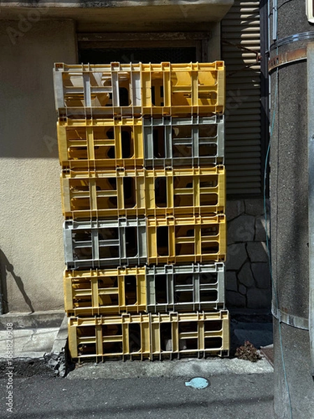 Fototapeta Plastic crates stacked against a wall. Urban life concept. Handheld mobile photo, selective focus, harsh sunlight, non AI