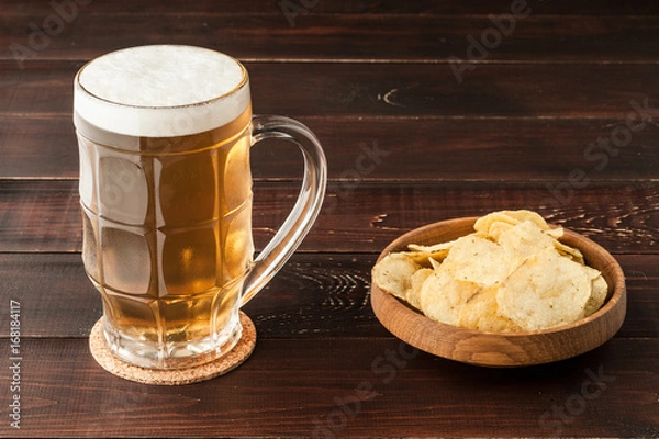 Fototapeta glass of cold frothy lager beer and potato chips plate on wooden table