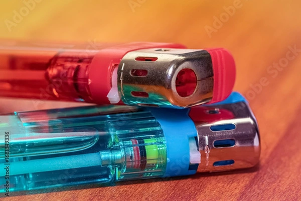 Fototapeta Two red and blue plastic lighters are resting on a wooden surface , photographed in close-up