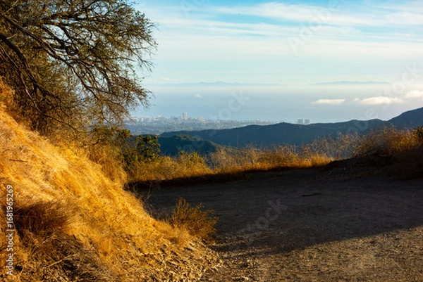 Fototapeta A shot of a hiking trail through the Santa Monica Mountains with a distant and hazy view of the Los Angeles cityscape