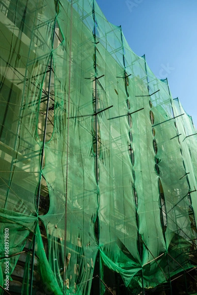 Fototapeta A shot of a building in Alexandria covered in a web of green scaffolding and netting, representing the ongoing urban development of the city