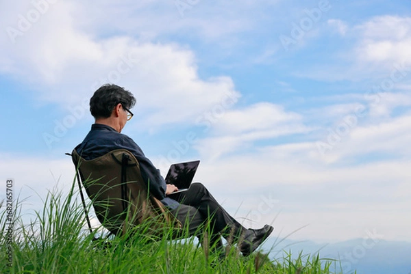 Obraz これからの働き方　草原でパソコンを広げる男性