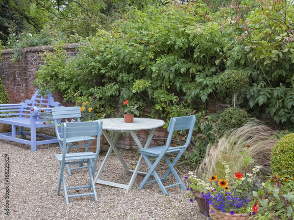 Obraz Blue bench, patio table and chairs by a wall in an English cottage garden, summertime .
