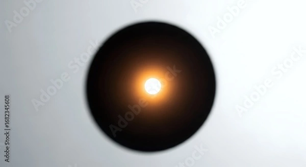 Fototapeta A vibrant light sphere glows warmly in the center of a dark, abstract circular shape, contrasted against a clean, light grey background. Perfect for minimalist and modern aesthetics.