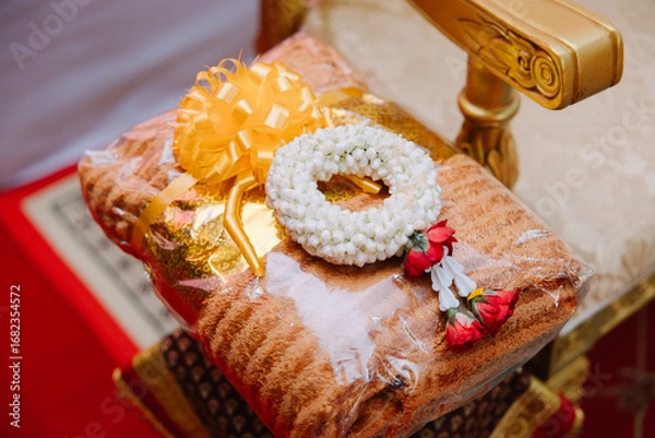 Obraz Close-up of a stack of orange monk's robes, neatly folded on an ornate silver pedestal, with other elements in the background.