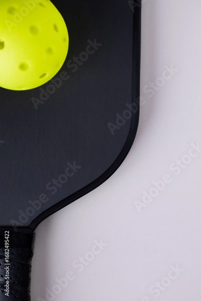 Fototapeta Close-up of a black pickleball paddle and neon yellow ball on a light background with copy space. Sport gear concept with minimalist aesthetic.