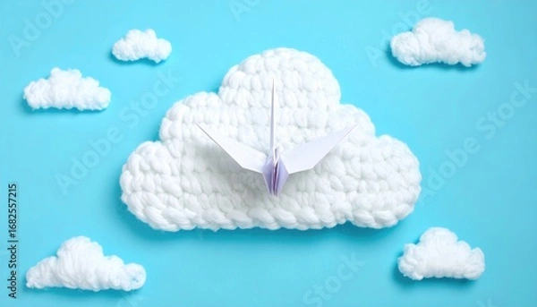 Fototapeta A paper origami bird soars from a fluffy, crocheted cloud surrounded by smaller clouds on a bright cyan background. Peaceful, simple, clean composition