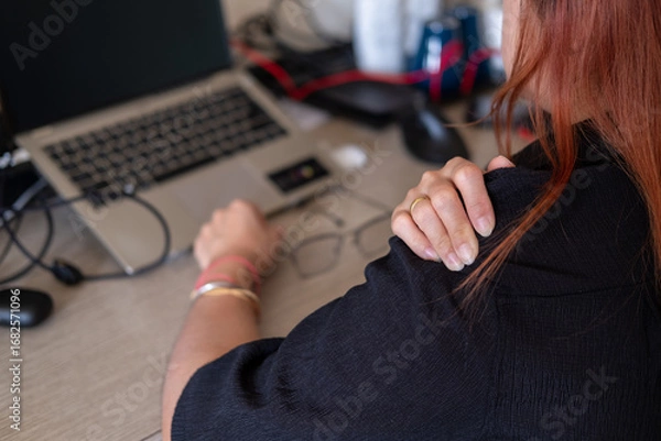 Fototapeta Hands rubbing aching shoulders in office setting with laptop and work equipment nearby