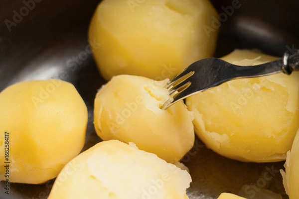 Fototapeta A fork piercing boiled peeled potatoes, close-up
