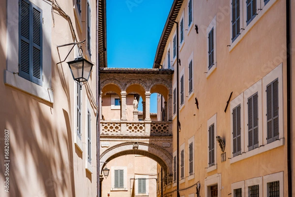 Fototapeta Low angle view of a charming bridge adorned with a statue, connecting buildings in Spoleto, Italy, showcasing traditional architecture and creating a scenic urban landscape