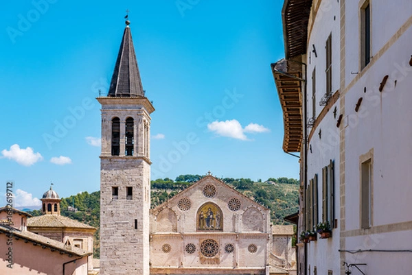Fototapeta Rising majestically against rolling green hills and a clear blue sky, the Spoleto Cathedral's intricate facade and towering bell tower create a picturesque view of this historic Italian city