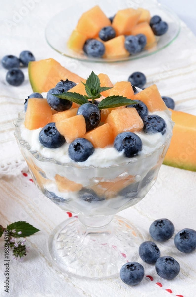 Fototapeta Glass bowl with yogurt, melon, blueberries, mint on a light table.Selective focus.