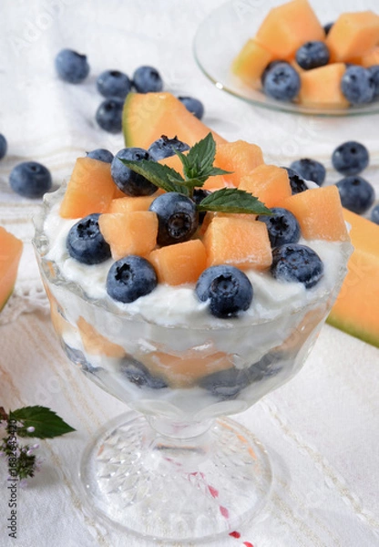 Fototapeta Glass bowl with yogurt, melon, blueberries, mint on a light table.Selective focus.
