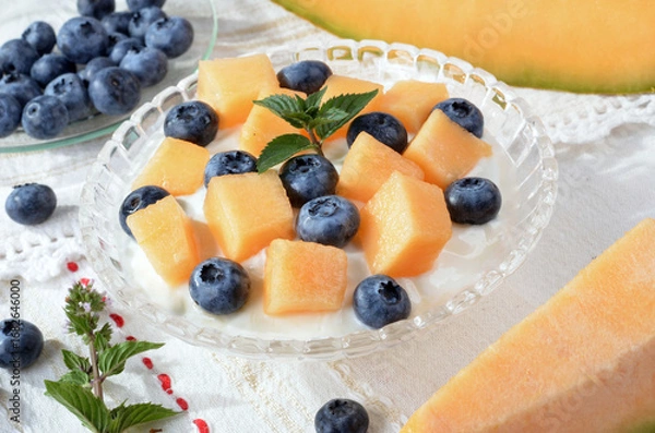 Fototapeta Glass bowl with yogurt, melon, blueberries, mint on a light table.Selective focus.