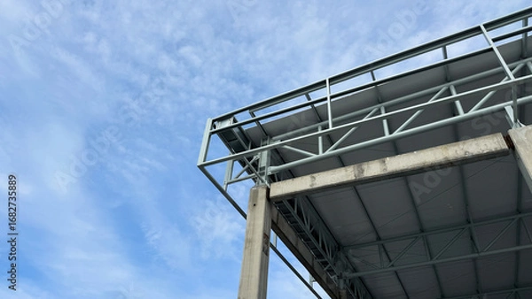 Fototapeta Corner view of concrete column and steel truss roof structure under construction with clear blue sky background, modern architecture and civil engineering detail.
