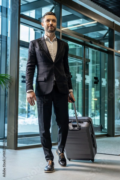 Fototapeta Man in formal wear carrying a suitcase while entering the business center