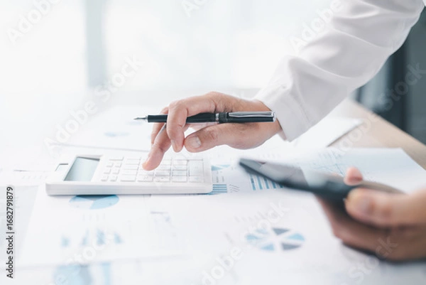 Fototapeta Concept of financial planning and accounting. A businesswoman uses a calculator to analyze reports and charts, calculating budget and investment strategy with focus and precision at office desk.