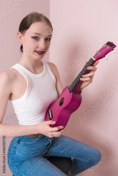 Fototapeta Young woman musician in positive light, holding ukulele. Her face conveys joy and she is looking at camera with sincere smile. Her positive facial expression conveys sense of cheer and friendliness