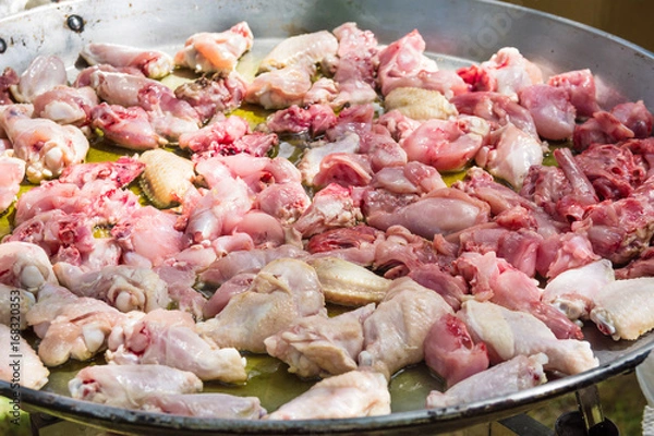 Fototapeta Process of frying rabbit and chicken juicy meat slices in olive oil in large flat paella skillet. Burner with open fire. Weekend picnic setting, summer. Lifestyle.