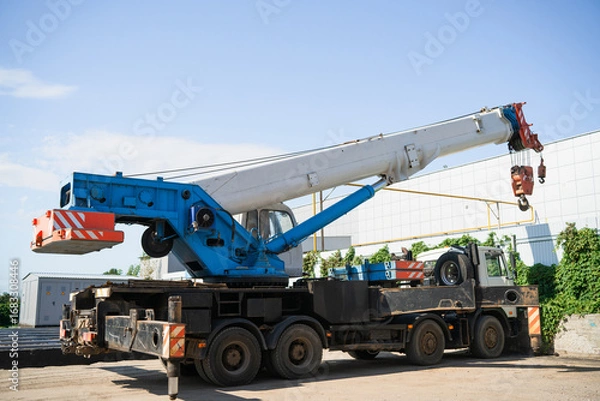Fototapeta A white and blue truck crane at a construction site is preparing for loading