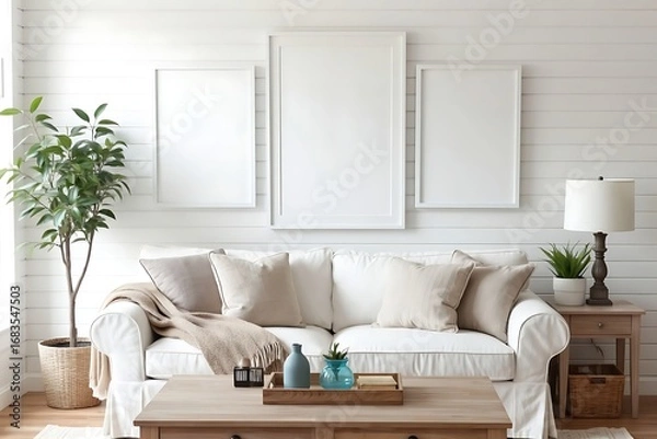 Fototapeta Bright modern farmhouse living room interior with a comfortable white slipcover sofa, wooden furniture, and blank frames on a shiplap wall.