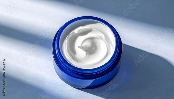 Fototapeta A glossy, cobalt blue jar of luxurious, creamy lotion sits atop a light blue surface, catching the light.