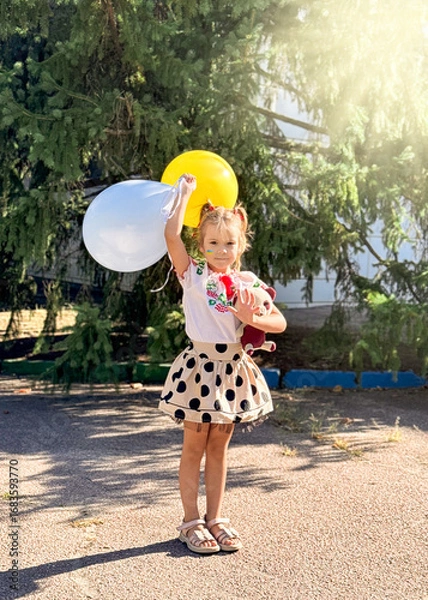 Fototapeta A girl holds two balloons, yellow and blue, at a summer party.