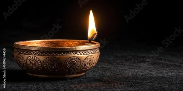 Fototapeta Ornate brass diya lamp with a bright flame on a dark textured surface