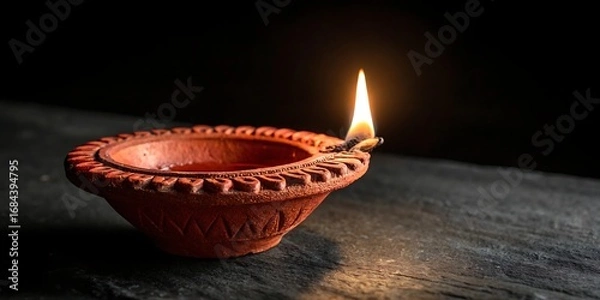 Fototapeta Single lit diya lamp on a dark wooden surface