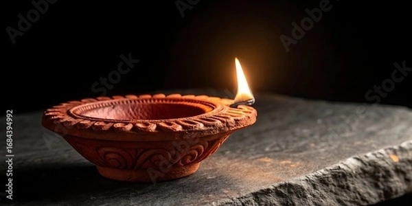 Fototapeta Illuminated clay diya lamp on a textured surface