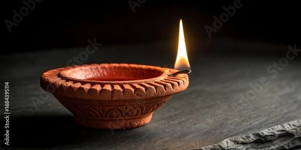 Fototapeta Single clay diya lamp with a bright flame on a dark background