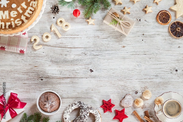 Fototapeta New year preparation concept. Christmass background with berries, cake, cup of coffee, red christmas tree toys. New Year composition candies, cinnamon, number year 2018 on a beige wooden background.