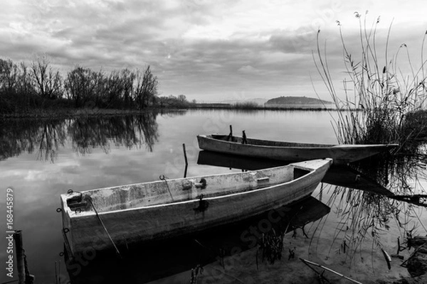 Obraz Some small fishing boats on a lake at almost sunset, with beautiful sky and clouds reflections on still water