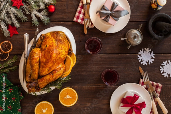 Fototapeta Festive table on christmas holidays served for two persons. Cone, dried oranges, plates, knife, fork furry spruce on a table. Top view. Baked chicken as a main dish.
