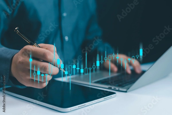 Fototapeta Businessman analyzing stock market candlestick chart on tablet and laptop, representing trading, investment, financial analysis, digital economy, and modern business technology in finance investment