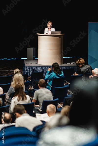 Fototapeta Female speaker giving a talk on corporate business conference. Unrecognizable people in audience at conference hall. Business and Entrepreneurship event