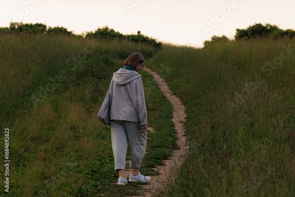 Fototapeta Walking along a grassy path during twilight in a peaceful outdoor setting