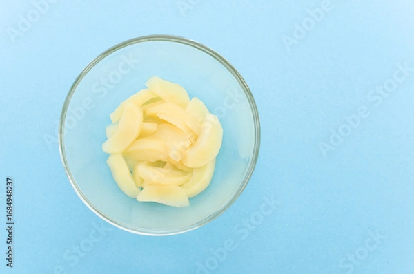 Fototapeta ciotola in vetro trasparente con mele cotte tagliate a fettine su sfondo azzurro chiaro con spazio vuoto