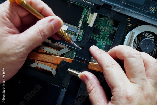 Obraz Computer repair technician, laptop motherboard repair technician uses a screwdriver to disassemble computer components to remove them for replacement and repair.
